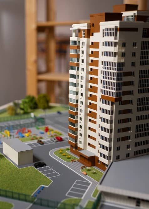 Scale model of a urban development showing high-rise buildings, detailed streets, and miniature trees and vehicles, set against a backdrop of shelves in a softly lit environment at Estate Industry Page image in the Tanyo CRM webiste.