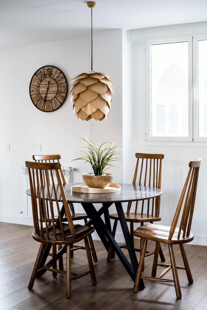 Modern dining room with a round table and four wooden chairs, an ornate pendant light, a large round clock on the wall, and a window providing natural light at Furniture Industry Page image in the Tanyo CRM webiste.